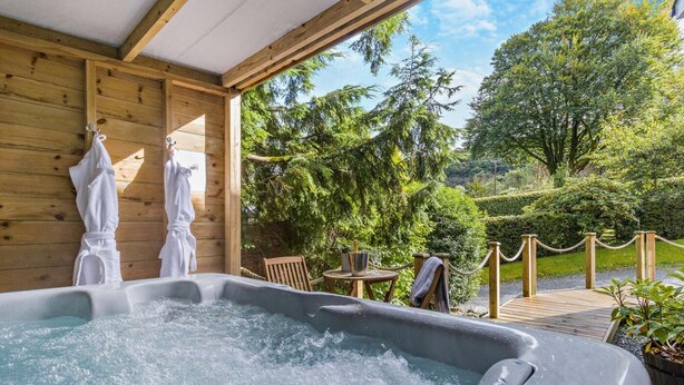 Ett bubbelbad med träväggar och utsikt över en trädgård med träd och en träaltan.