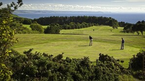 En golfbana med utsikt över havet och berg i bakgrunden.