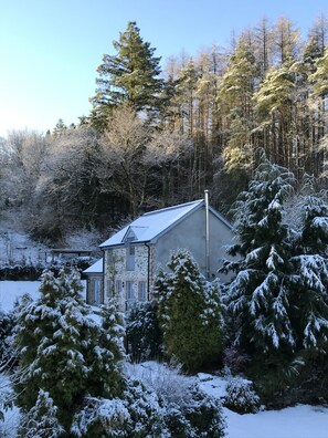 Een stenen gebouw met een schuin dak, omgeven door met sneeuw bedekte bomen en een heldere lucht.