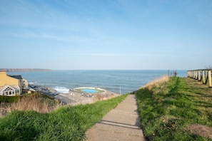 A coastal walkway leading to a beach with a pool and a view of the sea. - 4 Bed in Filey (oc-sa018) (Filey)