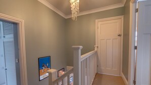 Ein Korridor mit einem Chandelier, einer weißen Tür und gerahmten Bildern an der Wand.