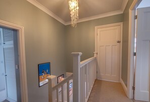 A hallway with a chandelier, a white door, and framed pictures on the wall. - 4 Bed in Filey (oc-sa018) (Filey)