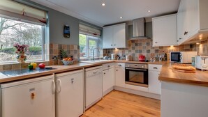 Eine moderne Küche mit weißen Schränken, einem eingebauten Ofen, einer Mikrowelle und einem Spülbecken. Der Rückwand ist mit farbenfrohen Fliesen versehen, und ein Fenster mit Jalousien sorgt für Licht.