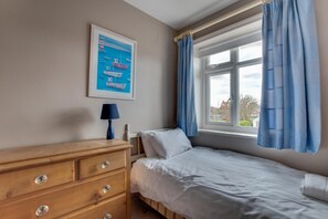 A bedroom with a wooden dresser, a bed, a window with blue curtains, and a painting on the wall. - 4 Bed in Filey (oc-sa018) (Filey)