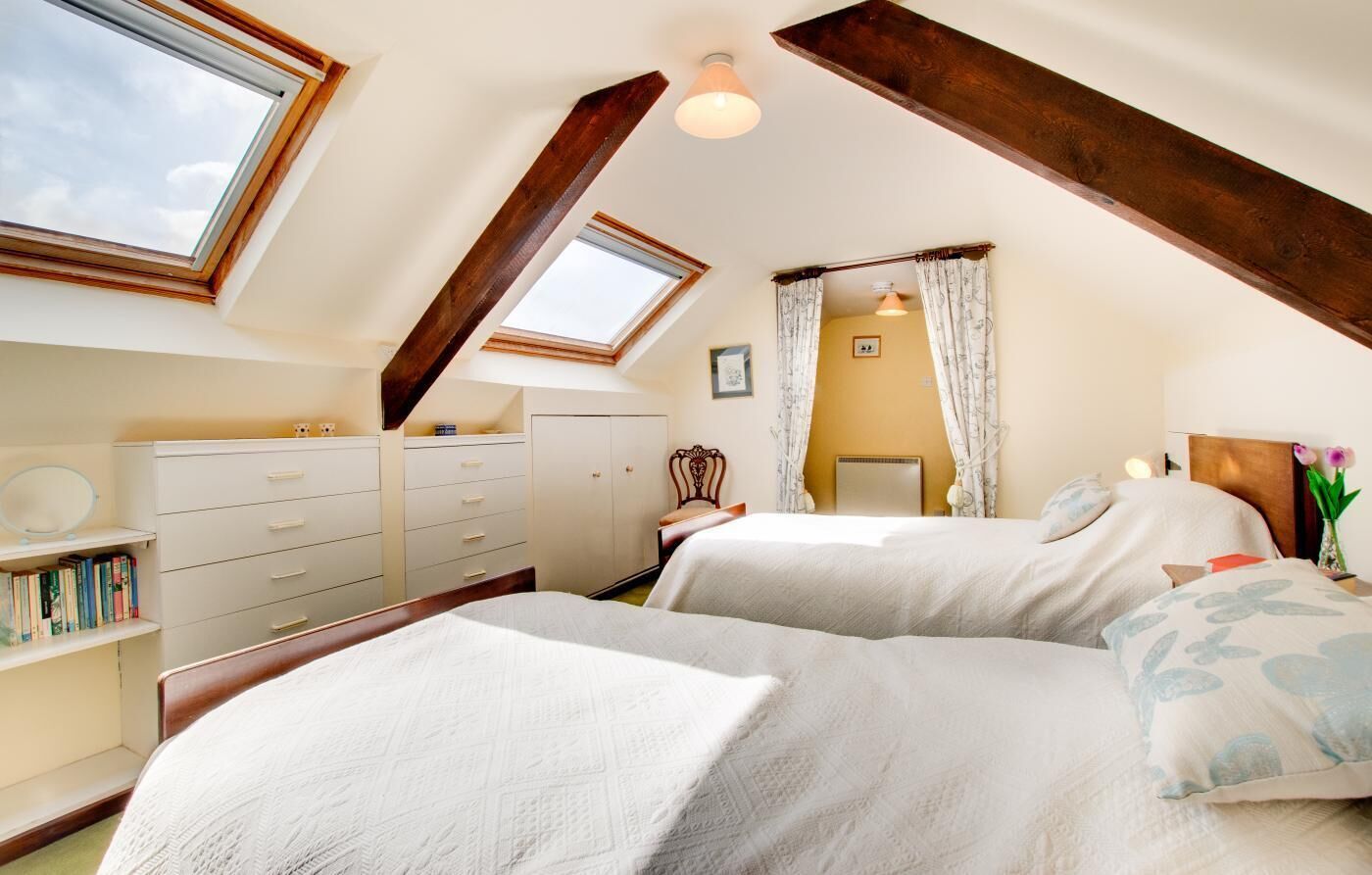 A bedroom with two beds, a skylight, a wardrobe, and a bedside table with a lamp.