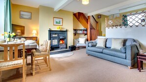 A cozy living room with a fireplace, a sofa, a dining table with chairs, and a staircase. - 2 Bed in Berwick-upon-Tweed (oc-nb678) (Lowick)