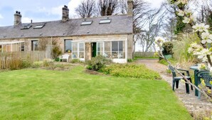 A stone house with a conservatory, a lawn, and a garden with flowers. - 2 Bed in Berwick-upon-Tweed (oc-nb678) (Lowick)