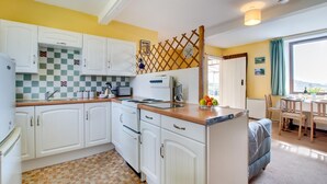 A compact kitchen with white cabinets, a checkered backsplash, and a small dining area with a table and chairs. - 2 Bed in Berwick-upon-Tweed (oc-nb678) (Lowick)