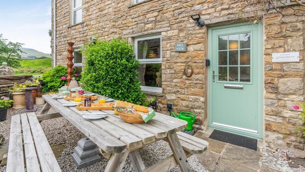 Un edificio de piedra con una puerta verde, una mesa de picnic con comida y un letrero que dice 'Hill View'.