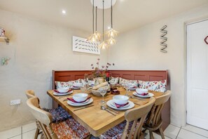 A dining room with a wooden table set for four, chairs, a decorative vase, and a modern light fixture.