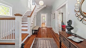 A spacious hallway with a wooden staircase, a bench, and a rug. - Historic Comfort l Walk to DNTN l Fire Pit (St. Augustine)