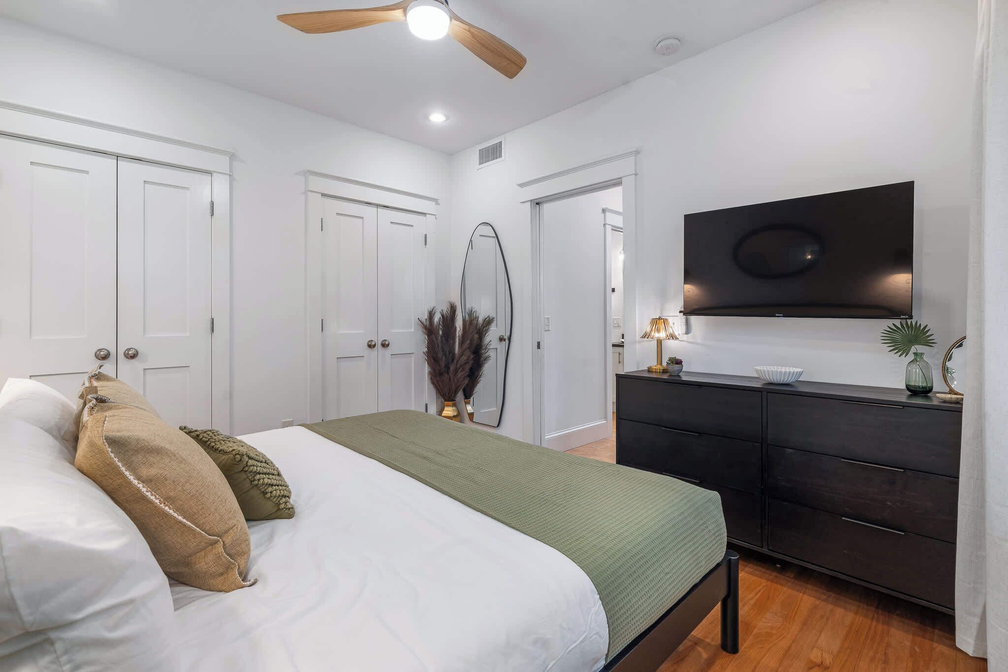 Une chambre à coucher comprenant un lit, une commode, un téléviseur fixé au mur et un ventilateur de plafond.