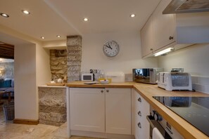 Eine moderne Küche mit Säule aus Stein, weißen Schränken, einer Mikrowelle, einem Toaster und einer Uhr an der Wand.