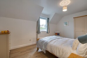 A bedroom with a bed, a window, a radiator, a wardrobe, and a chair.