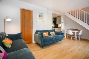 Una sala de estar moderna con un sofá azul, una puerta de madera y un comedor con sillas blancas y una mesa.