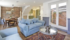 Ein geräumiges Wohnzimmer mit einem blauen Sofa, einem Esstisch mit Stühlen und einem großen Fenster mit Blick nach draußen.