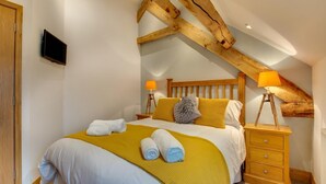 Een slaapkamer met een bed, twee nachtkastjes, een houten hoofdbord en een aan de muur bevestigde televisie.