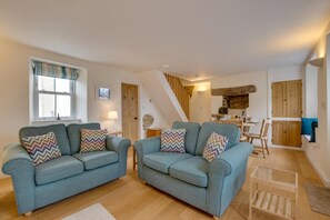 A spacious living area with two sofas, a dining table, and a staircase leading to an upper level. - 2 Bed in Porthleven (oc-pevcot) (Porthleven)
