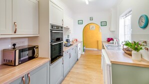 Eine moderne Küche mit weißen Schränken, einem eingebauten Backofen und einer Mikrowelle. Es gibt eine Holz Arbeitsplatte, ein Spülbecken und ein Fenster mit einer Uhr.
