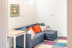 A modern living room with a grey sectional sofa, colorful cushions, a small white table, and a colorful rug. - 3 Bed in Scarborough (oc-s018) (Scarborough)