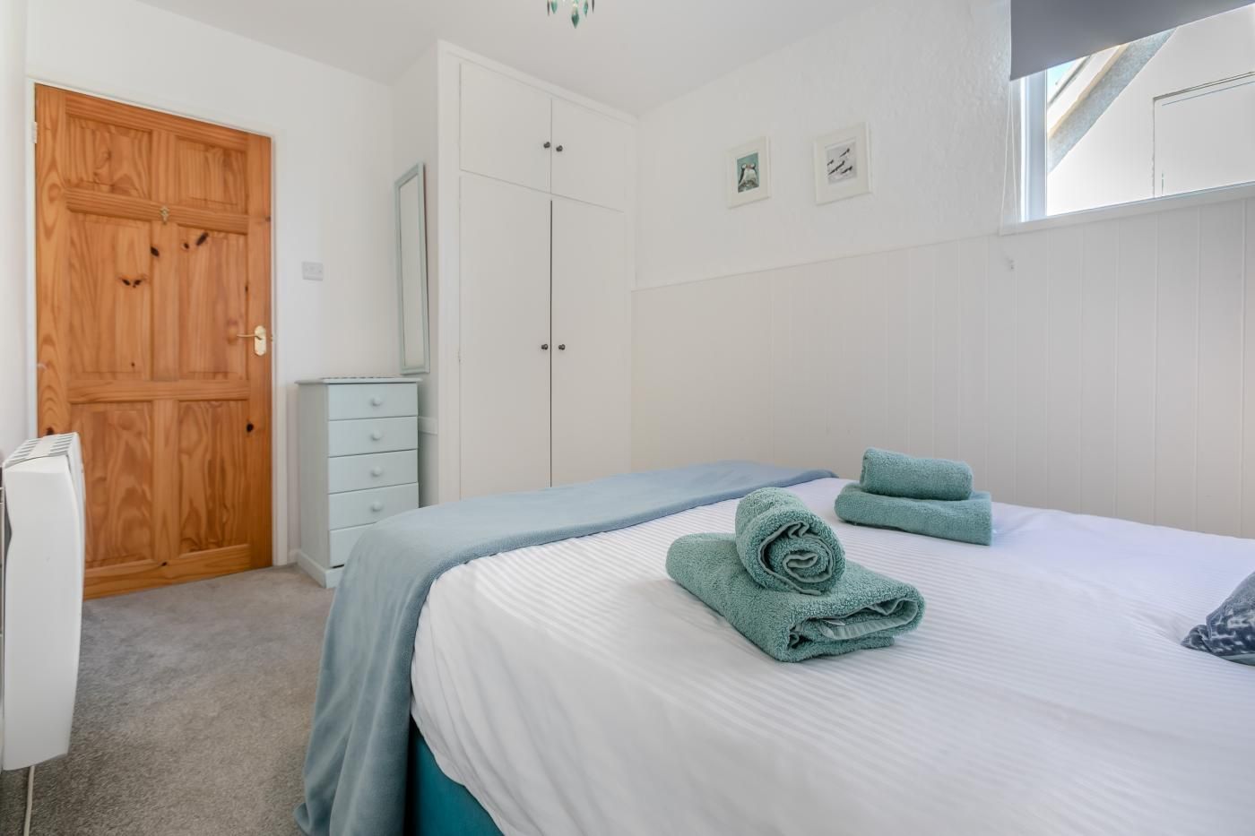 Une chambre à coucher avec un lit, une armoire en bois, une commode blanche et un miroir.