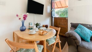 Un comedor con una mesa redonda de madera, sillas, un jarrón de flores, un televisor montado en la pared y un reloj en la pared.