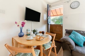 A dining area with a round wooden table, chairs, a vase of flowers, a television mounted on the wall, and a clock on the wall.