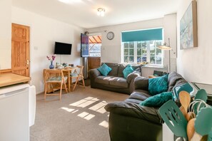 A cozy living room with a sofa, a dining table with chairs, a television, and a window with a view.