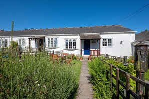 A white building with a blue door, a garden with a wooden fence, and a pathway leading to the entrance.