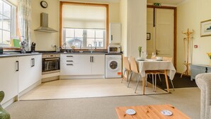 Une cuisine compacte équipée d’un évier, d’un four à micro-ondes, d’un four et d’un lave-linge. On y trouve également un coin repas avec une table et des chaises, ainsi qu’un petit coin salon avec un canapé.