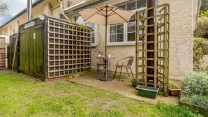 Une terrasse avec une table et des chaises, un portail en bois et un petit jardin.