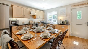 A modern kitchen with wooden cabinets, a dining table set for six, and a view of the outdoors through a window. - 3 Bed in Beadnell (oc-44965) (Beadnell)