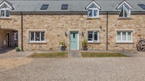 A stone building with a central entrance, two windows on either side, and a small porch area. - 3 Bed in Beadnell (oc-44965) (Beadnell)