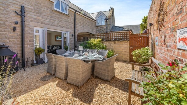 A stone building with a patio area featuring wicker furniture and a table set for dining. - 3 Bed in Beadnell (oc-44965) (Beadnell)