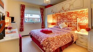 A bedroom with a floral-patterned bedspread, a chandelier, and a view of a building outside the window. - 2 Bed in Beadnell (oc-79928) (Beadnell)