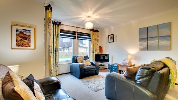 A living room with a sofa, a blue armchair, a television, and a fireplace. - 2 Bed in Beadnell (oc-79928) (Beadnell)