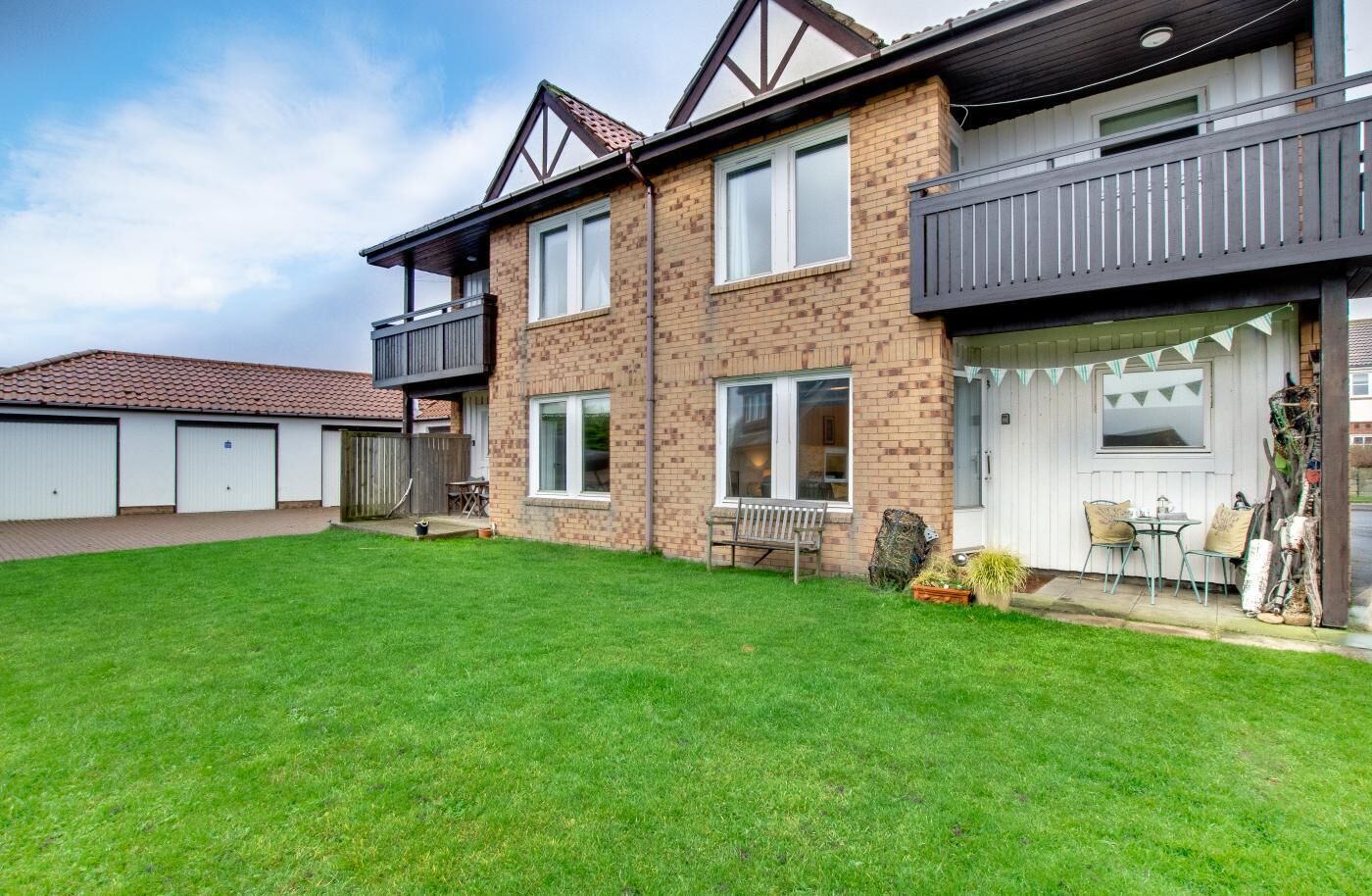 A two-story residential building with a well-maintained lawn, a balcony, and a small patio area with outdoor seating.