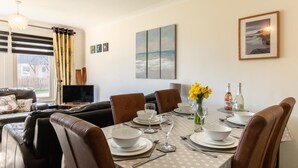 A dining area with a table set for four, surrounded by leather chairs, a vase of yellow flowers, and a painting on the wall. - 2 Bed in Beadnell (oc-79928) (Beadnell)