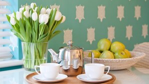 Ein Tisch mit einem Teekessel, Tassen, einem Strauß Tulpen und einem Korb voller Äpfel.