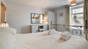 Ein Schlafzimmer mit Bett, Kommode, Spiegel und einem Fenster mit Vorhängen.
