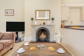 Una sala de estar con chimenea, un sofá, una mesa de centro con tazas y aperitivos, un televisor y una zona de cocina con fregadero y encimera.
