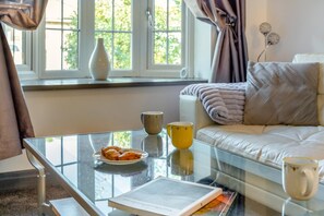 Ein modernes Wohnzimmer mit einem Glastisch, einer Couch mit Decke und einem Fenster mit Vorhängen.
