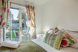 A bedroom with a bed, a nightstand, a lamp, and a view of an outdoor patio with chairs and a table. - 2 Bed in Seahouses (oc-373002) (Seahouses)