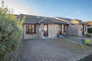 A stone house with a tiled roof, a paved driveway, and a small garden area with potted plants. - 2 Bed in Seahouses (oc-373002) (Seahouses)