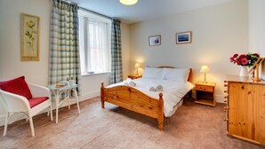 Une chambre à coucher avec un lit en bois, une chaise blanche, une petite table, une table de chevet avec une lampe et une armoire en bois.