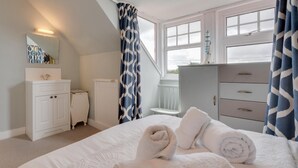 Un dormitorio con cama, cómoda, espejo y ventana con cortinas.
