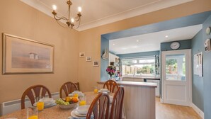 Un comedor con una mesa dispuesta para cuatro personas, una cocina con ventana y una puerta que da al exterior.