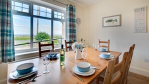 Comedor con una mesa dispuesta para cuatro, vista al exterior y un cartel con las 'Normas de la Casa'.