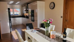 Una cocina moderna con armarios blancos, una mesa de comedor con cuatro sillas, un florero con flores y un reloj en la pared.