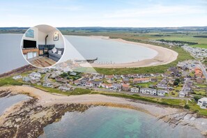 An aerial view of a coastal village with a beach, houses, and a small harbor. - 5 Bed in Beadnell (oc-24955) (Beadnell)
